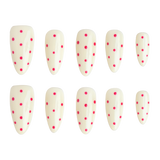 Ten false press-on nails arranged in two rows of five on a plain white background. The nails are glossy off-white with small bright pink polka dots scattered across the surface.