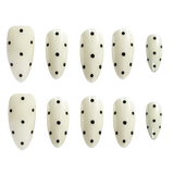 Ten almond-shaped press-on nails with a glossy off-white finish and black polka dots, arranged in two rows of five on a plain white background.