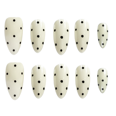 Ten almond-shaped press-on nails with a glossy off-white finish and black polka dots, arranged in two rows of five on a plain white background.