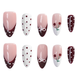 Ten almond-shaped press-on nails arranged in two rows of five on a plain white background. The nails feature various designs: pink-to-white gradient with dark burgundy tips, white with burgundy dots, white with a white bow motif, pink-to-white gradient with cherry details, and dark burgundy with white dots.