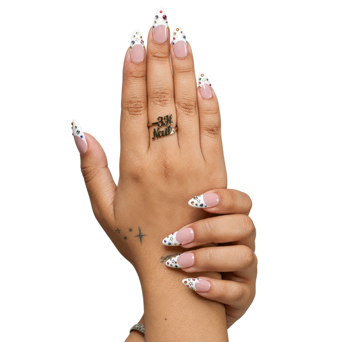 Dallas medium almond press-on nails by 3H Nails, featuring a nude base with white French tips, multicolor rhinestones, and gold star accents, shown in a lifestyle image.