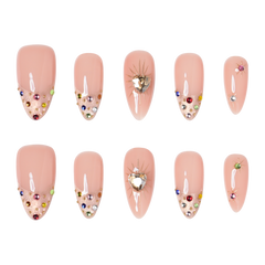 Boston medium almond press-on nails by 3H Nails, featuring a nude base with champagne glitter, multicolor gems, metallic accents, and heart details.